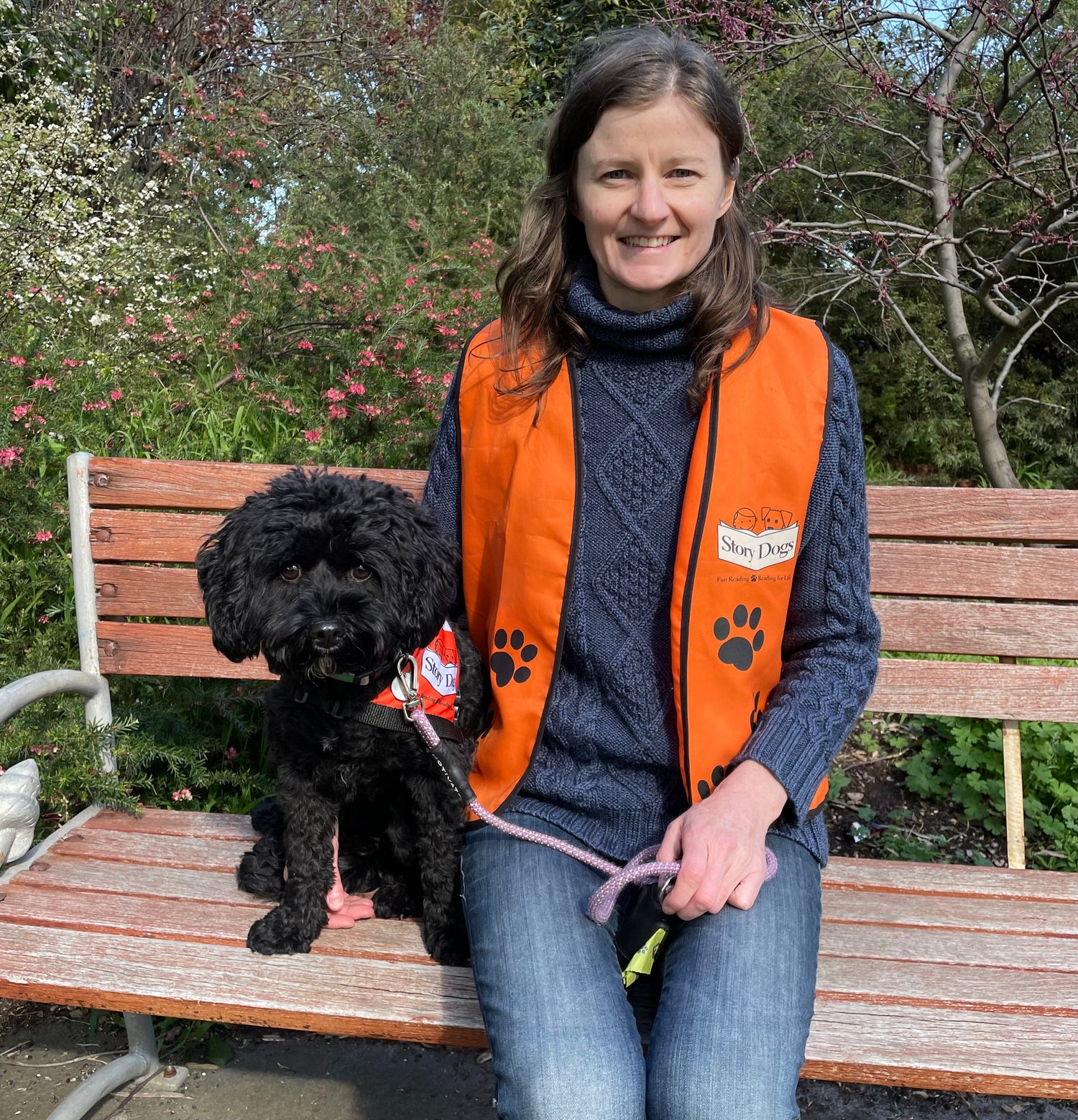 Woman in an orange vest with a black dog on a bench in a garden